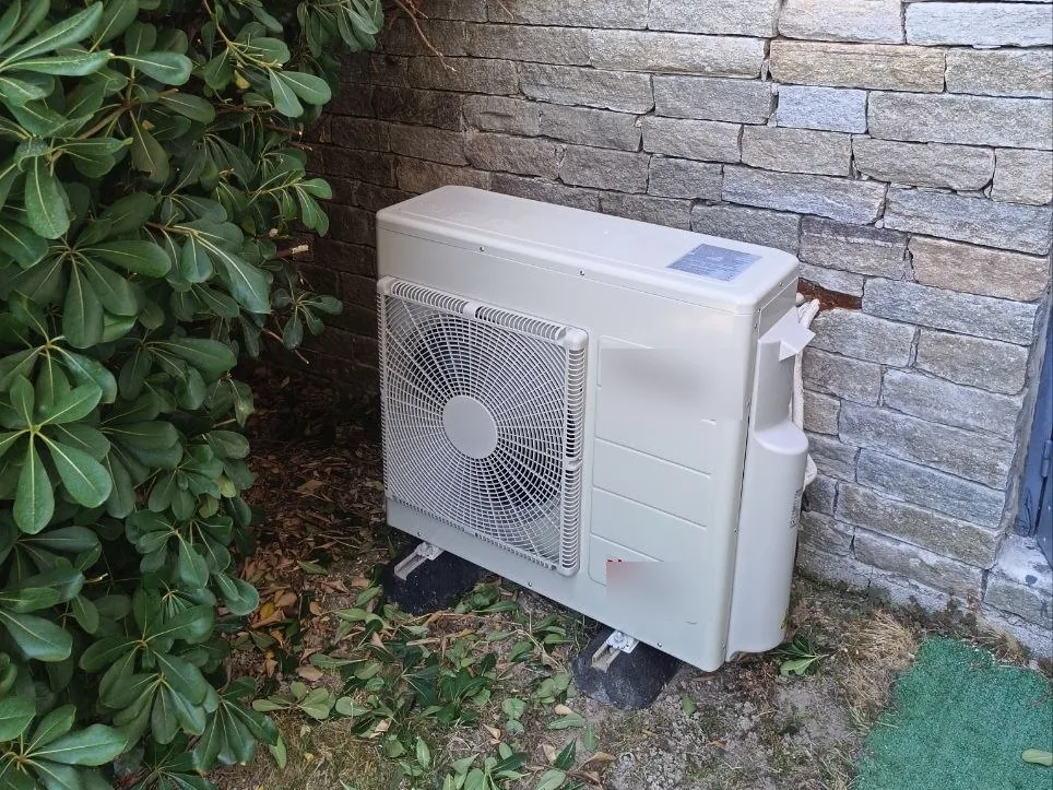 Unité extérieure de climatisation posée sur des supports au pied d'un mur en pierre
